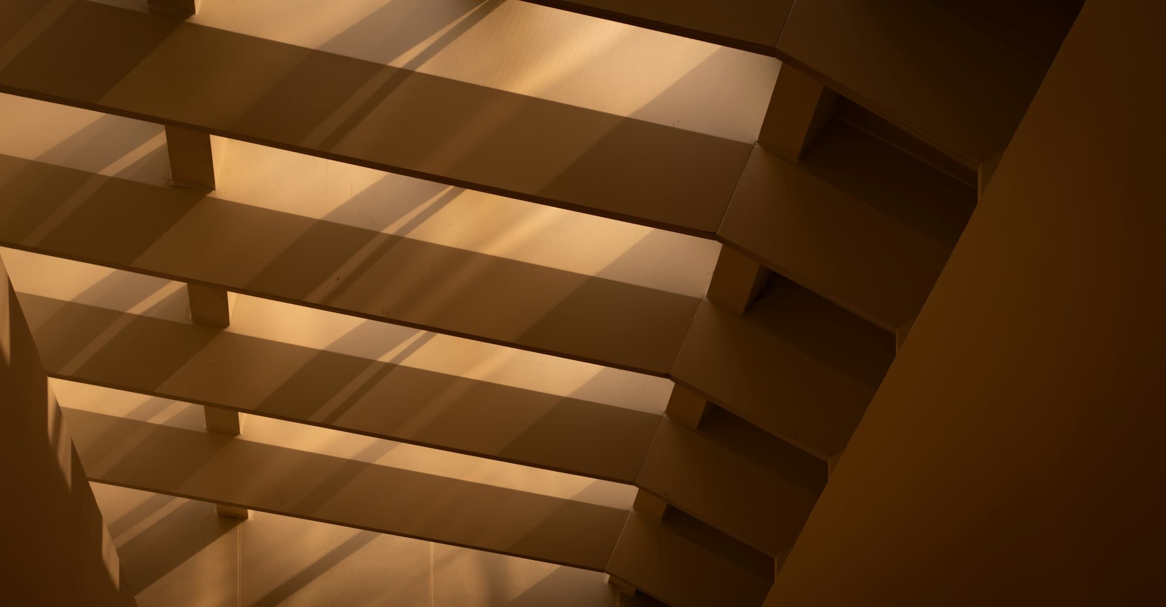 Architectural detail of horizontal floor slabs in a stairwell, lit by warm raking sunlight throwing diagonal shadows across each level